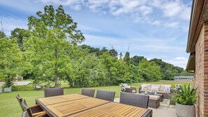 Eine Terrasse im Freien mit einem Holztisch und Korbstühlen, umgeben von Grünpflanzen und einer Backsteinmauer.