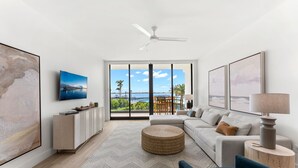 A modern living room with a large window, a ceiling fan, a sofa, a coffee table, and a TV mounted on the wall. - Newly Renovated | Luxe Condo w/ Riverfront Views, Pool & Resort Amenities! (Melbourne Beach)