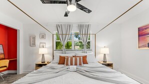 Una cama bien hecha con ropa de cama blanca, dos lámparas de noche y un ventilador de techo.