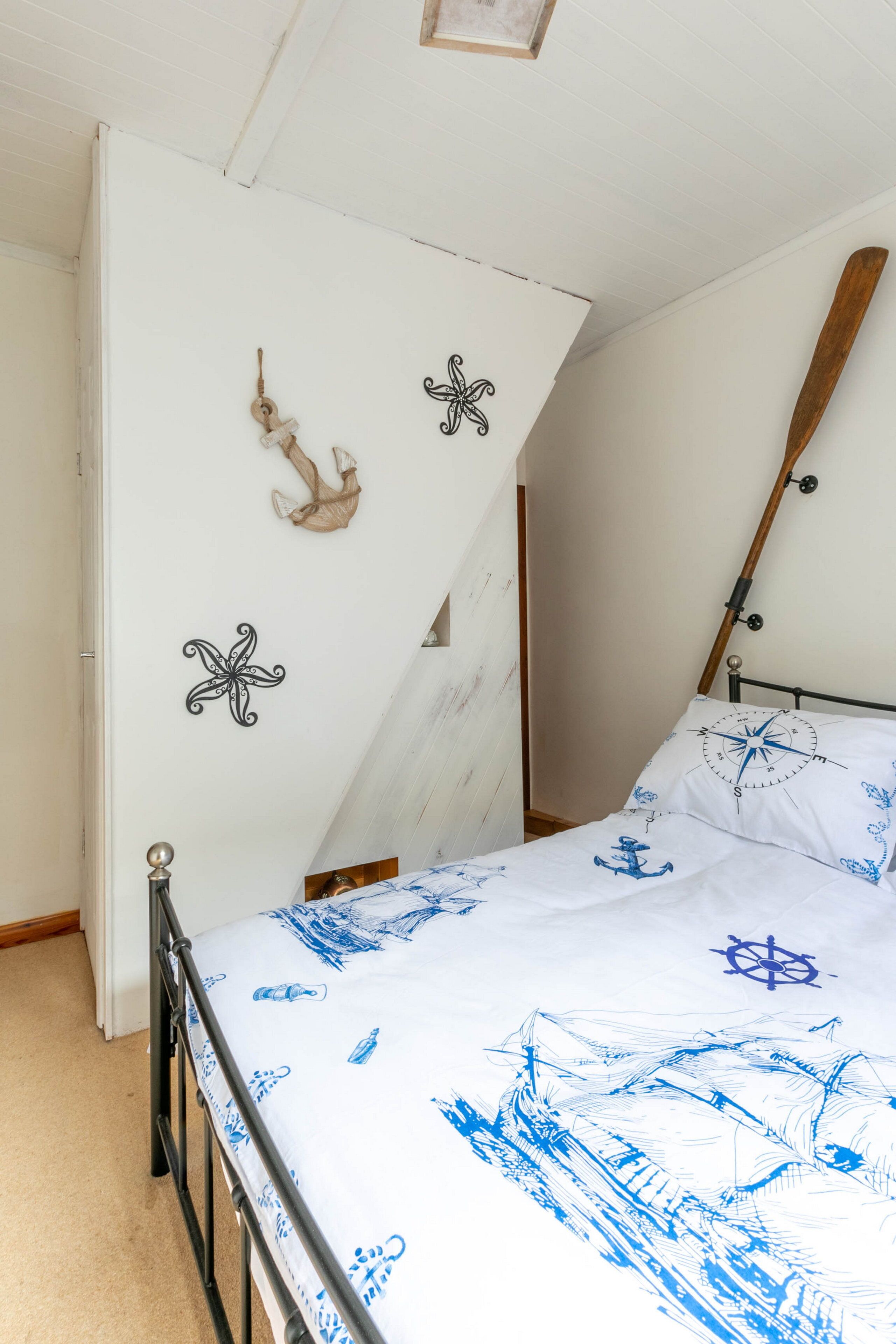 A bedroom with a bed, a wooden ceiling, and nautical-themed wall decorations.