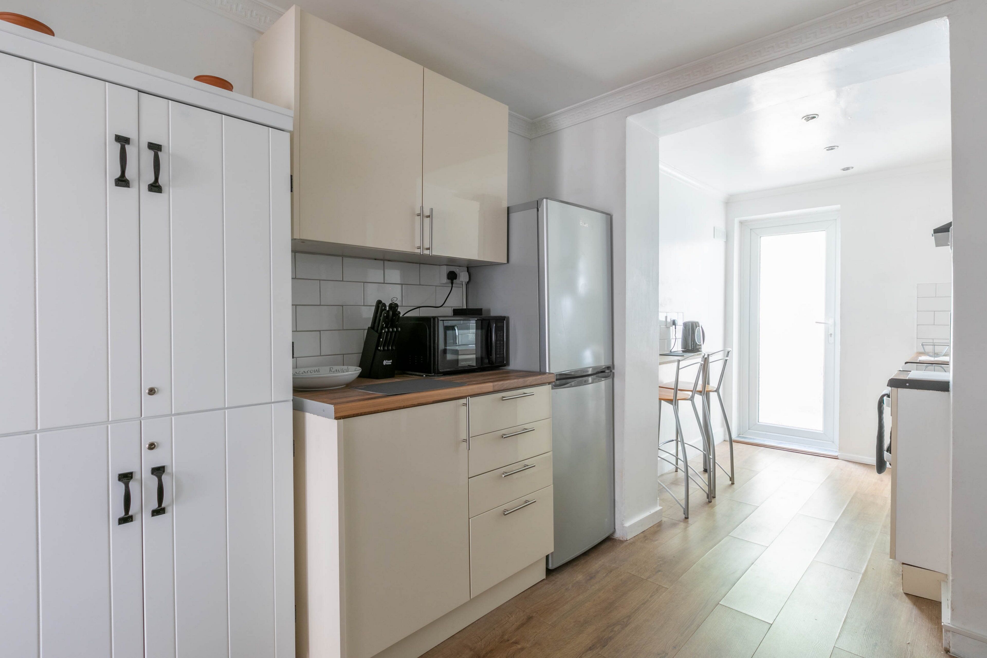 Une cuisine moderne avec des meubles blancs, un réfrigérateur en acier inoxydable et un plan de travail en bois.