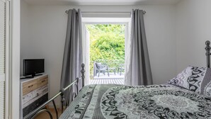 Una camera da letto con un letto, una TV su un comò e vista su un balcone con mobili da esterno.
