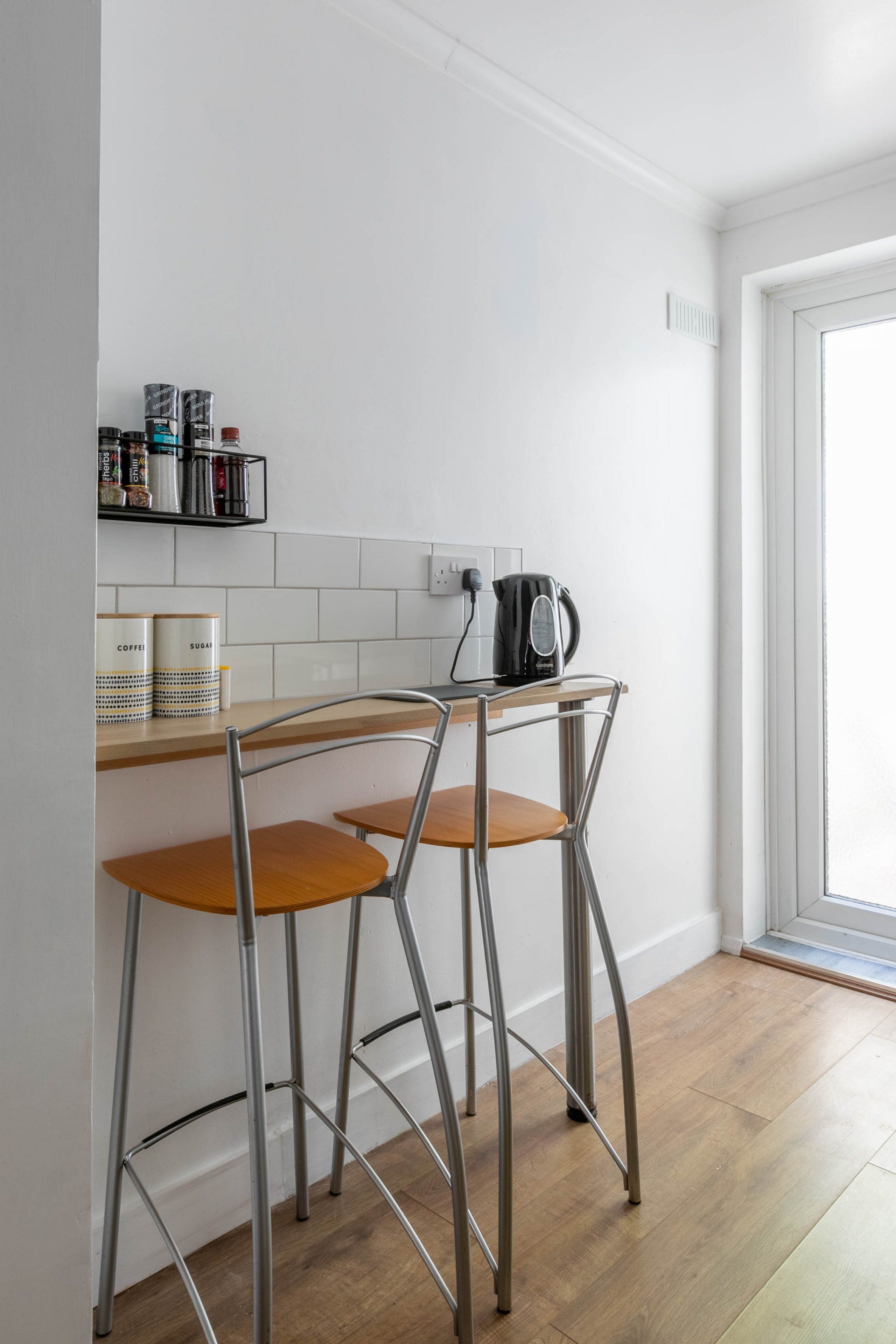 Eine moderne Küche mit zwei Barhocker, einer Kaffeemaschine und Aufbewahrungsbehältern auf der Arbeitsfläche.