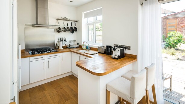 A modern kitchen with white cabinets, a wooden countertop, a gas stove, a sink, and a coffee maker. - Elegant 2Bd House With Garden And Decked Patio (London)