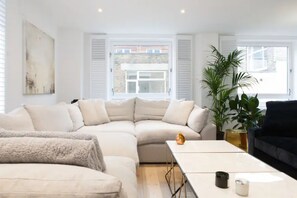 A modern living room with a sectional sofa, a coffee table, and a large plant. - Shoreditch - Immaculate 2 Bedrooms Flat For 6 (London)