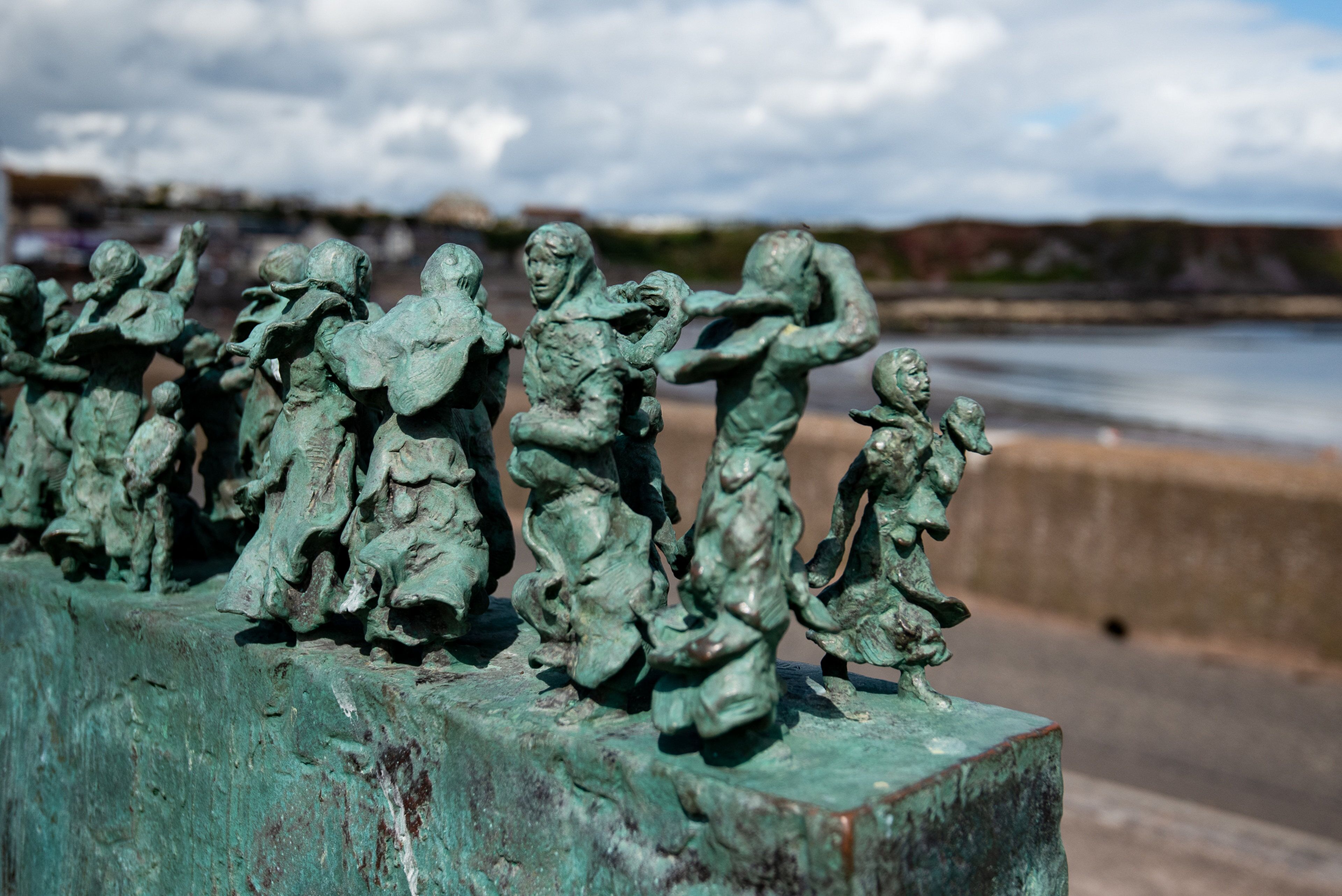 A row of bronze statues on a concrete ledge by the water.