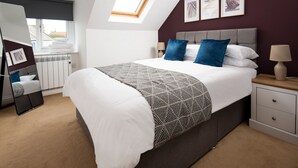 A modern bedroom with a large bed, a skylight, a bedside table with a lamp, and framed artwork on the wall. - Historic 2Bd Maisonette In Coastal Eyemouth (Eyemouth)