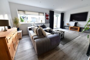 A modern living room with a sofa, a wooden cabinet, a TV, and a large window. - 2Bd Garden Home - A Short Walk To Stonehenge (Salisbury)