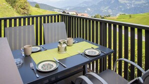 A dining table set outdoors with a mountain view, surrounded by chairs and a wooden railing. - La Siala Apt.51 by Interhome (Falera)