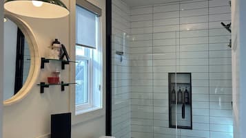 A modern bathroom with a white sink, a toilet, and a shower area. There is a window providing natural light, and the walls are tiled with a white pattern.