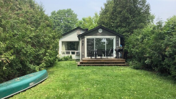 A small house with a deck and a canoe in the yard.
