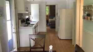 A compact kitchen with white cabinets, a dining area with a table and chairs, and a view into a bedroom.