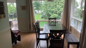 A dining area with a table and chairs, a hanging light fixture, and a view of a garden through large windows.