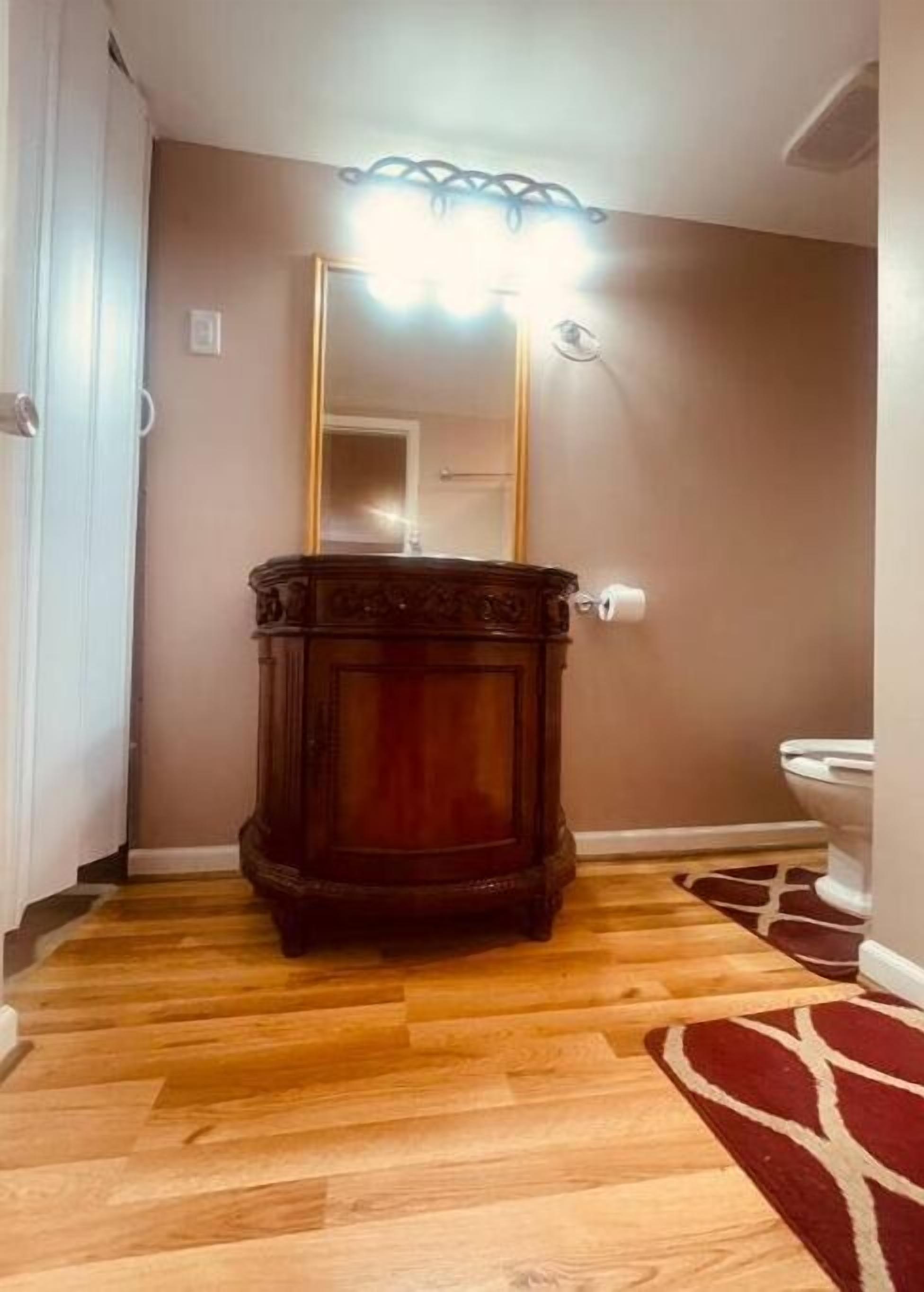 Ein Badezimmer mit einem Holzkosmetikschrank, einem Spiegel und einer Leuchte darüber.
