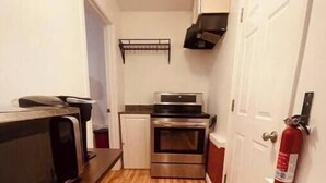 A narrow hallway with a wooden floor, a microwave, a small refrigerator, and a stove. - Garden Annex (North Garden)