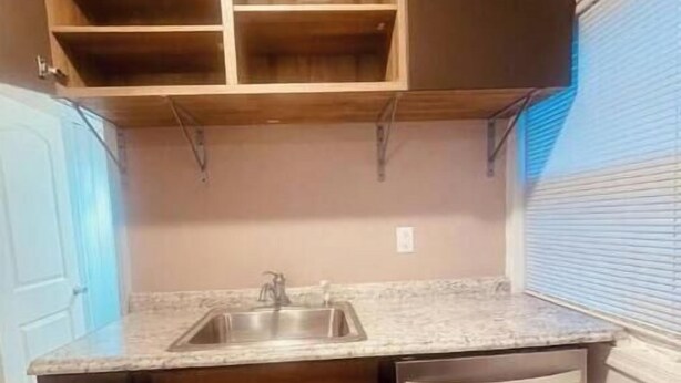 A kitchen with dark wooden cabinets, a granite countertop, and a built-in dishwasher. - Garden Annex (North Garden)