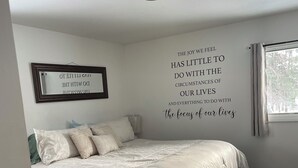 Une chambre à coucher avec un lit, un miroir, une citation inspirante sur le mur et une fenêtre.