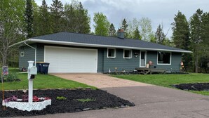 Une maison de plain-pied avec un garage, entourée d’un jardin aménagé et d’une allée.