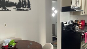 Une cuisine moderne équipée d’une cuisinière, d’un four et de placards. On y trouve une table à manger avec des chaises, et un panier rempli de divers objets posé dessus.