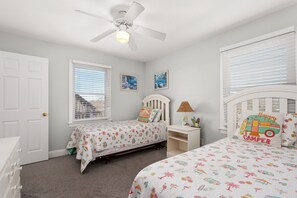 A bedroom with two beds, a ceiling fan, a window with blinds, and a door. - Gone Coastal: Private Pool, Hot Tub, Ocean and Sunset Views! (Nags Head)