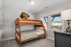 A bunk bed with a colorful floral bedspread, a fish decoration on the wall, and a window with a view of a house.