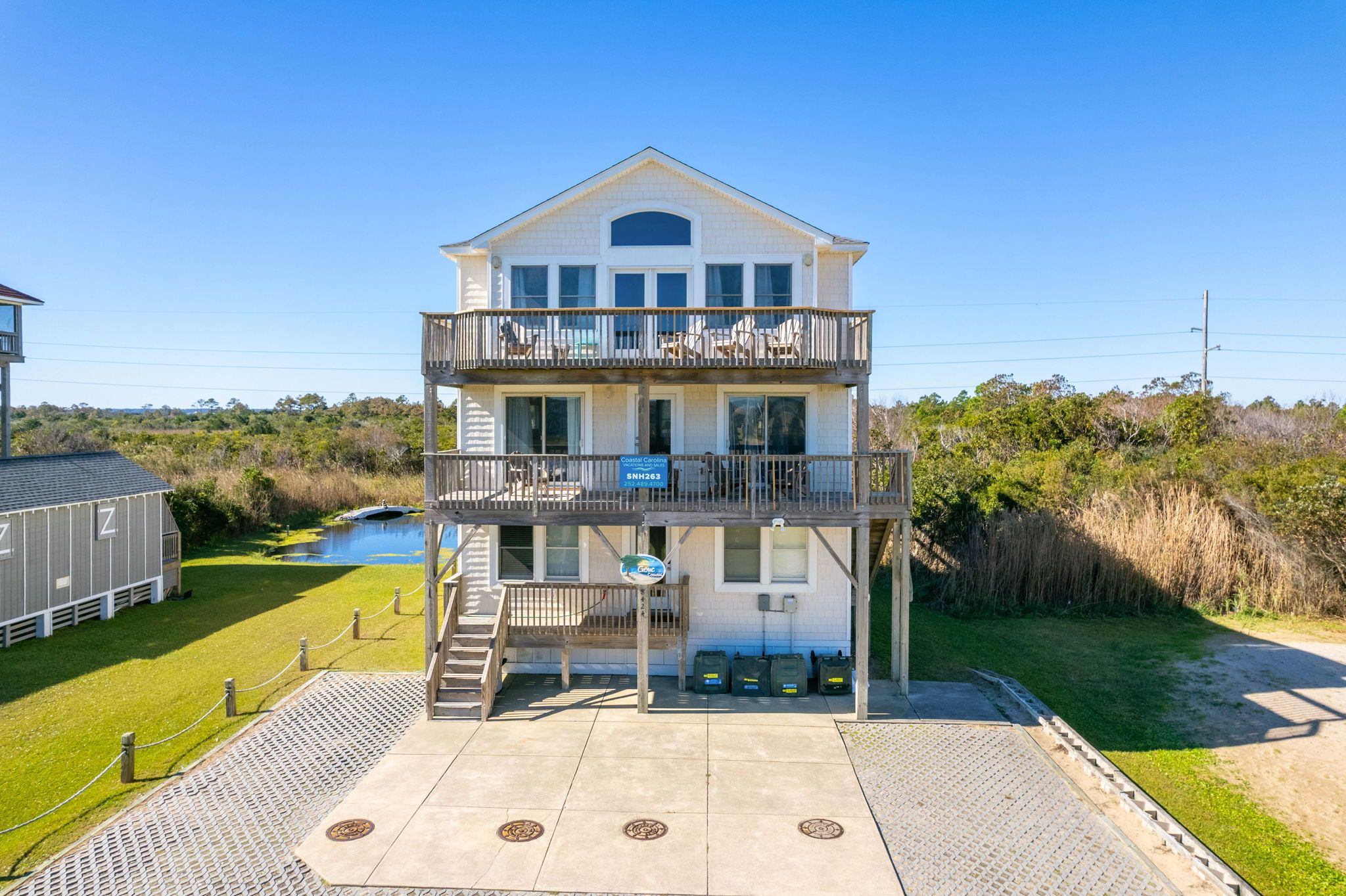 A two-story building with a balcony, a sign indicating it is a central coast property, and a small outdoor area with steps leading to the entrance.