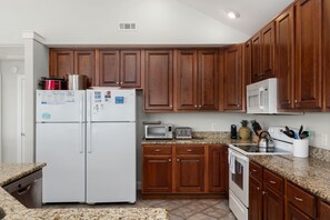 A kitchen with wooden cabinets, a white refrigerator, a microwave, a toaster, and a dishwasher. - Gone Coastal: Private Pool, Hot Tub, Ocean and Sunset Views! (Nags Head)