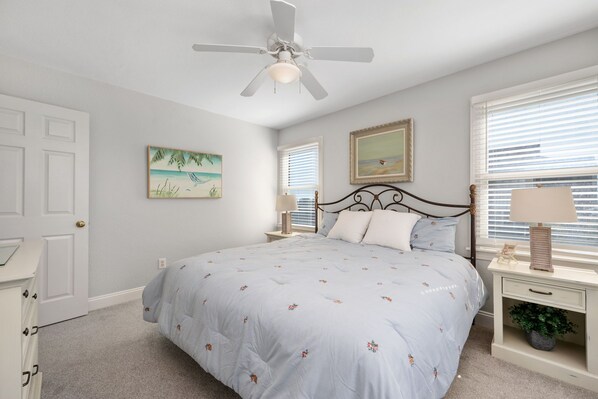 A bedroom with a bed, a ceiling fan, two bedside tables with lamps, a door, and a window with blinds.