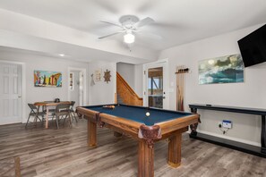 A pool table in a room with wooden flooring, a ceiling fan, and a TV mounted on the wall. - Gone Coastal: Private Pool, Hot Tub, Ocean and Sunset Views! (Nags Head)