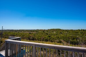 A wooden deck overlooking a landscape with dense greenery and a clear blue sky.
