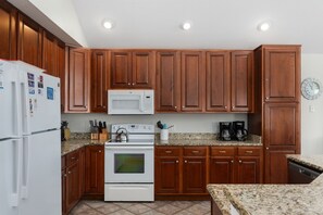 A kitchen with wooden cabinets, a white refrigerator, a microwave, a stove, and a coffee maker.