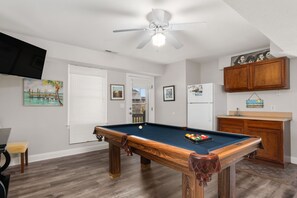 A pool table in a room with a ceiling fan, a refrigerator, wooden cabinets, and a TV mounted on the wall.