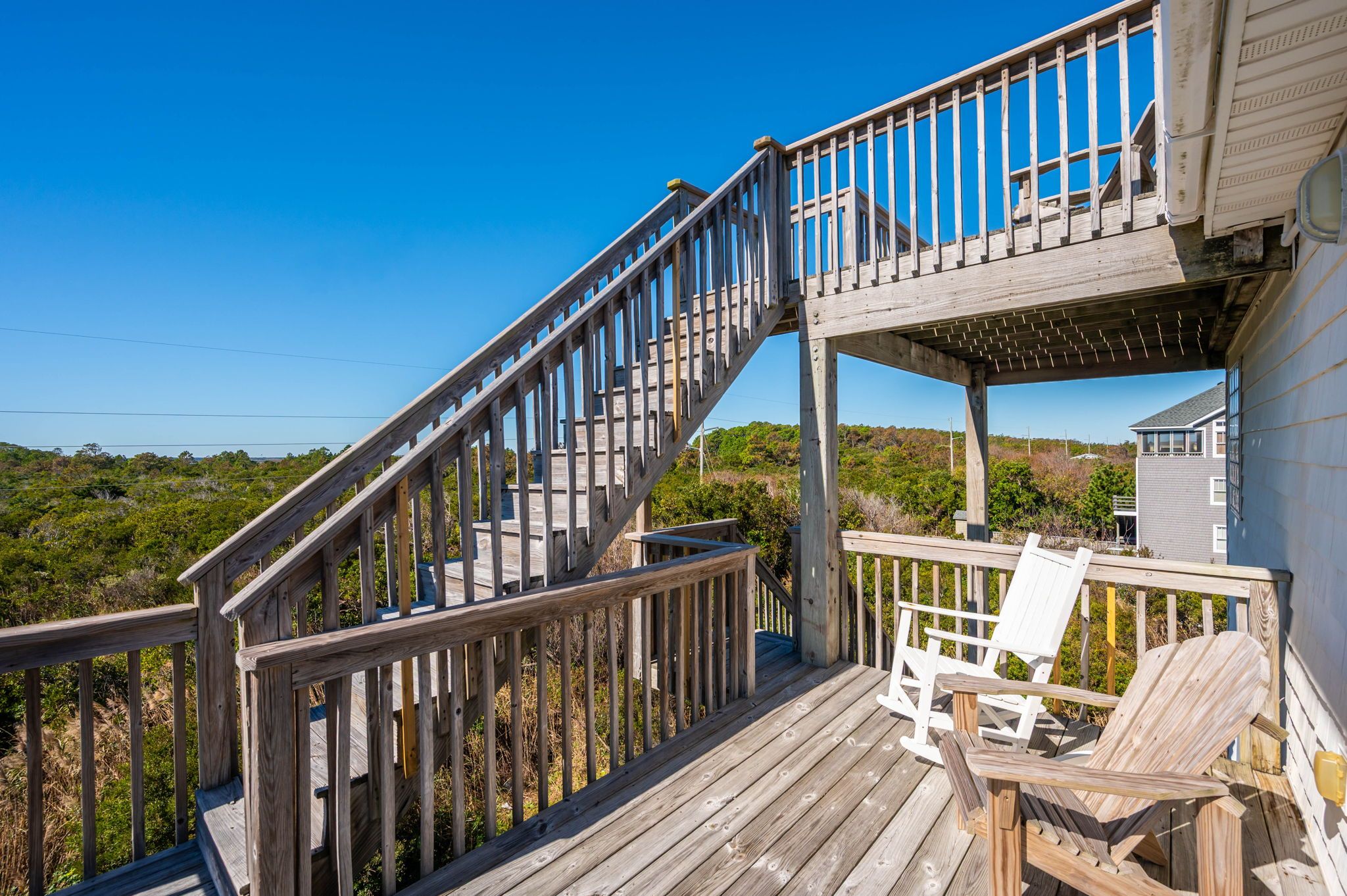 A wooden deck with a staircase leading to a covered area, surrounded by greenery.