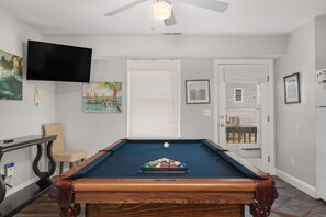 A pool table with balls, a television mounted on the wall, and a door leading to an outdoor area. - Gone Coastal: Private Pool, Hot Tub, Ocean and Sunset Views! (Nags Head)