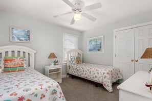 A bedroom with two beds, a ceiling fan, a nightstand, and a door. - Gone Coastal: Private Pool, Hot Tub, Ocean and Sunset Views! (Nags Head)