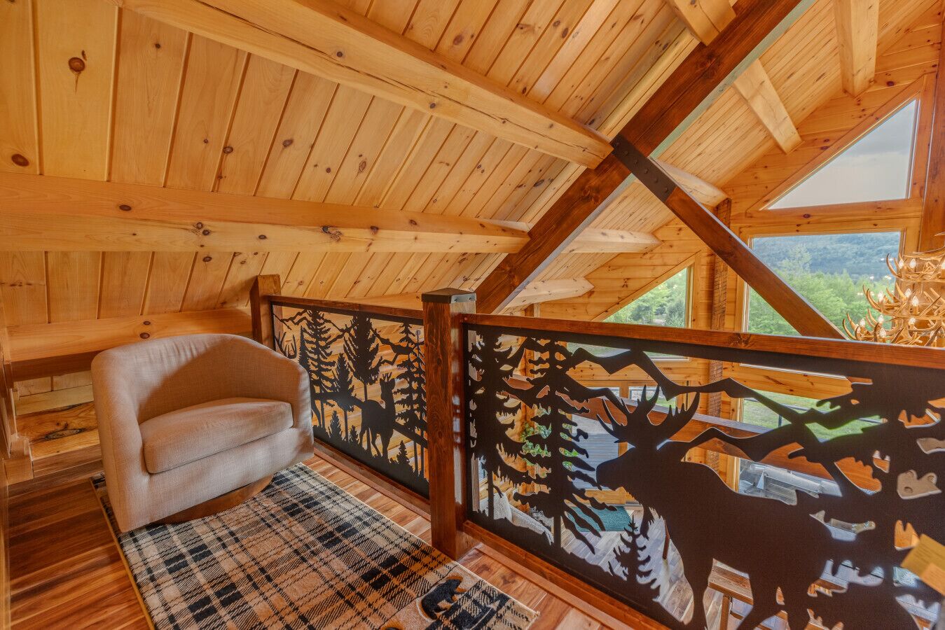 A cozy wooden cabin with a high ceiling, a plush sofa, a plaid rug, and a decorative metal fence with wildlife cutouts.