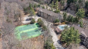 Ovenfra ses et område med tennisbane, swimmingpool og en bygning med balkon.