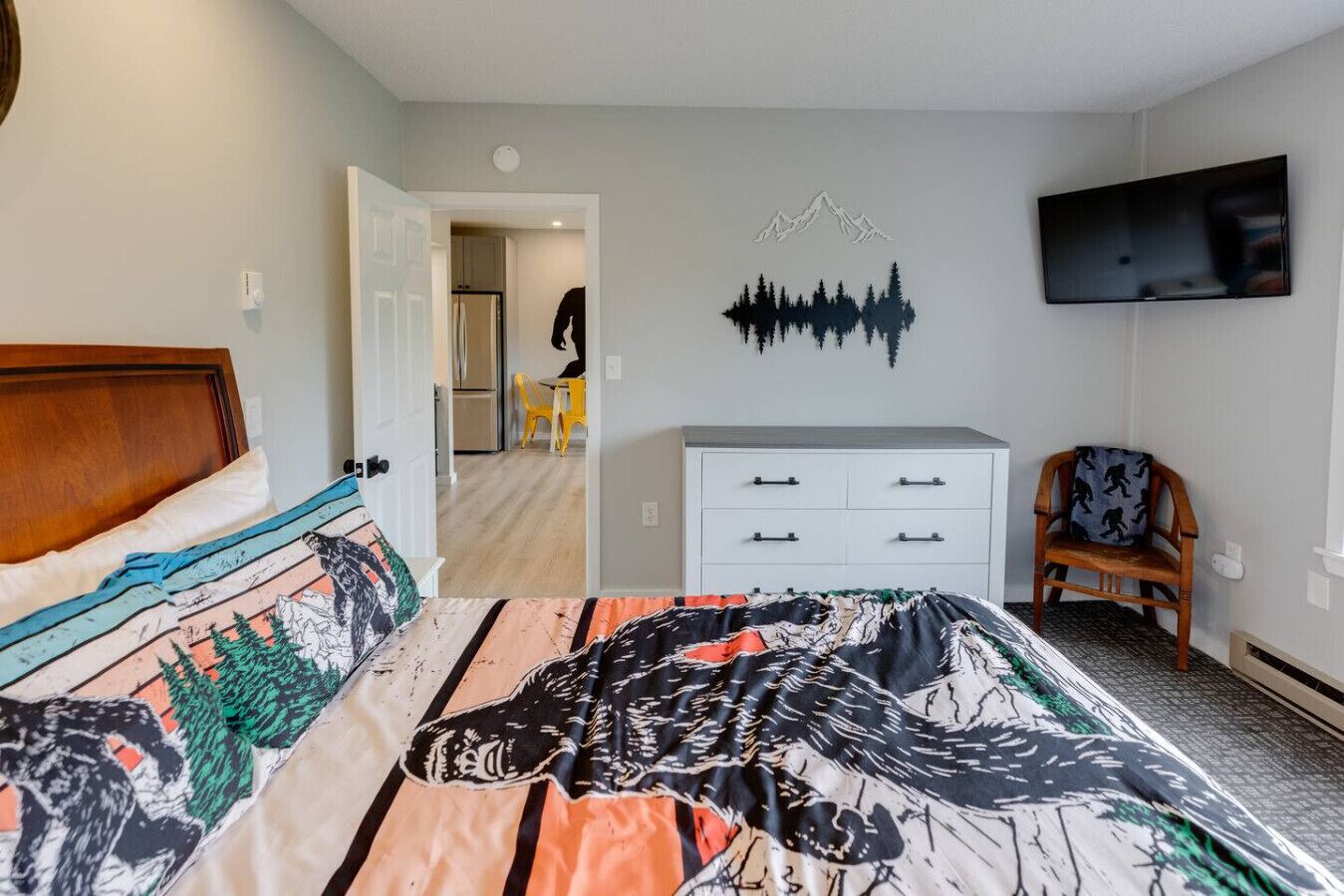 Ein Schlafzimmer mit einem Bett, einem Schminktisch, einem Sessel und einem Fernseher an der Wand.