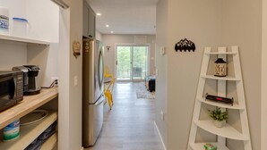 Una cocina moderna con refrigerador, microondas y cafetera. Se ve una silla amarilla al fondo.
