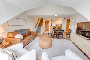 Un espacio habitable tipo loft con sofá, reposapiés, mesa de comedor, sillas y una zona de cocina.