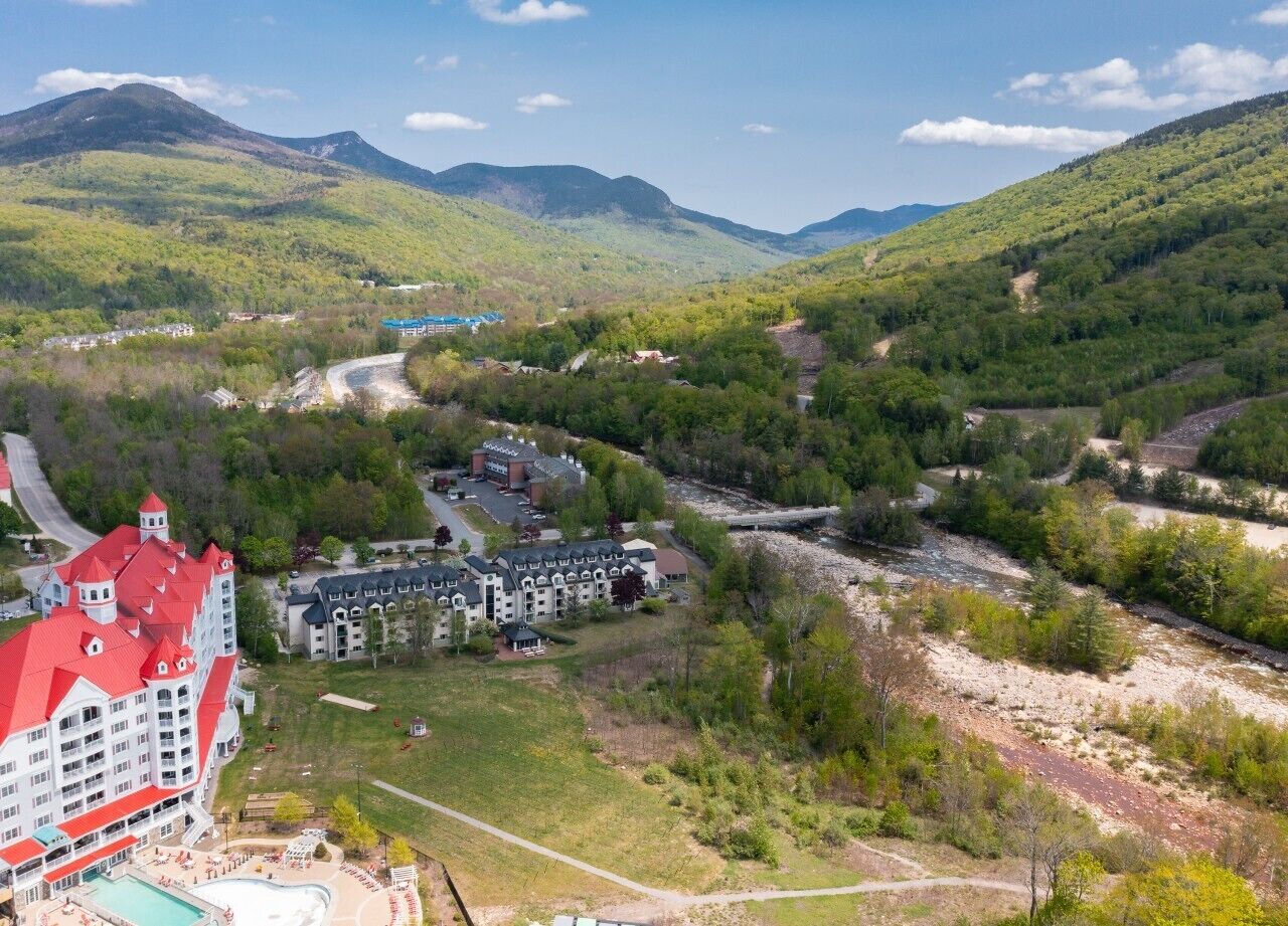 A hotel with a red-roofed building, a swimming pool, and a view of a valley with a river.