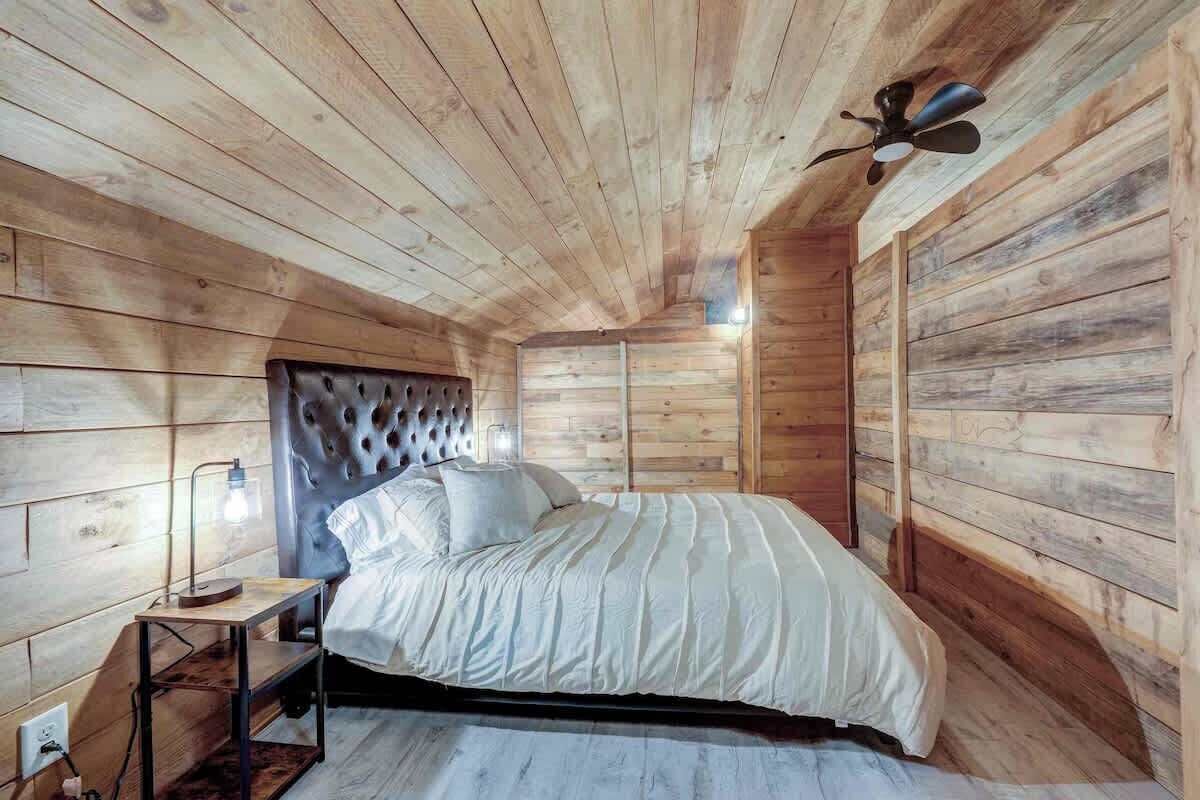 A wooden cabin bedroom with a bed, a nightstand, a lamp, and a ceiling fan.