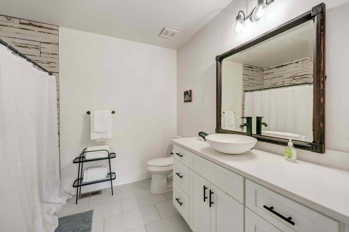 Une salle de bain avec un lavabo blanc, un grand miroir, un porte-serviettes et des toilettes.