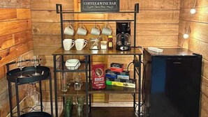 Un bar chaleureux où l’on sert du café et du vin, avec un décor intérieur en bois, une machine à café, un réfrigérateur et une étagère remplie de tasses et de mugs.