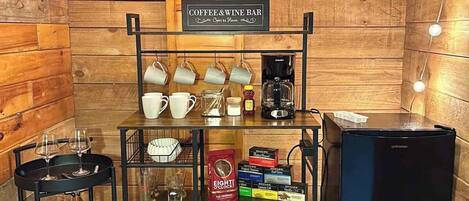 Un acogedor bar de café y vinos con interior de madera, una máquina de café, un refrigerador y una estantería con tazas y vasos.