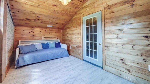 Une petite pièce agréable, avec un lit, un plafond en bois et une porte.