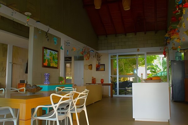 A spacious kitchen with a dining area, featuring a large island, white chairs, and various kitchen appliances.