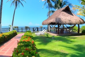 Un salon de plage doté d’un toit de chaume, d’un hamac et offrant une vue sur l’océan.