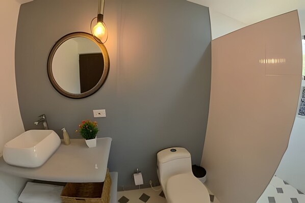 Un baño moderno con un lavamanos blanco, un espejo redondo y un inodoro.