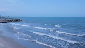 Une plage avec des vagues, une côte rocheuse et une jetée qui s’étend au loin.